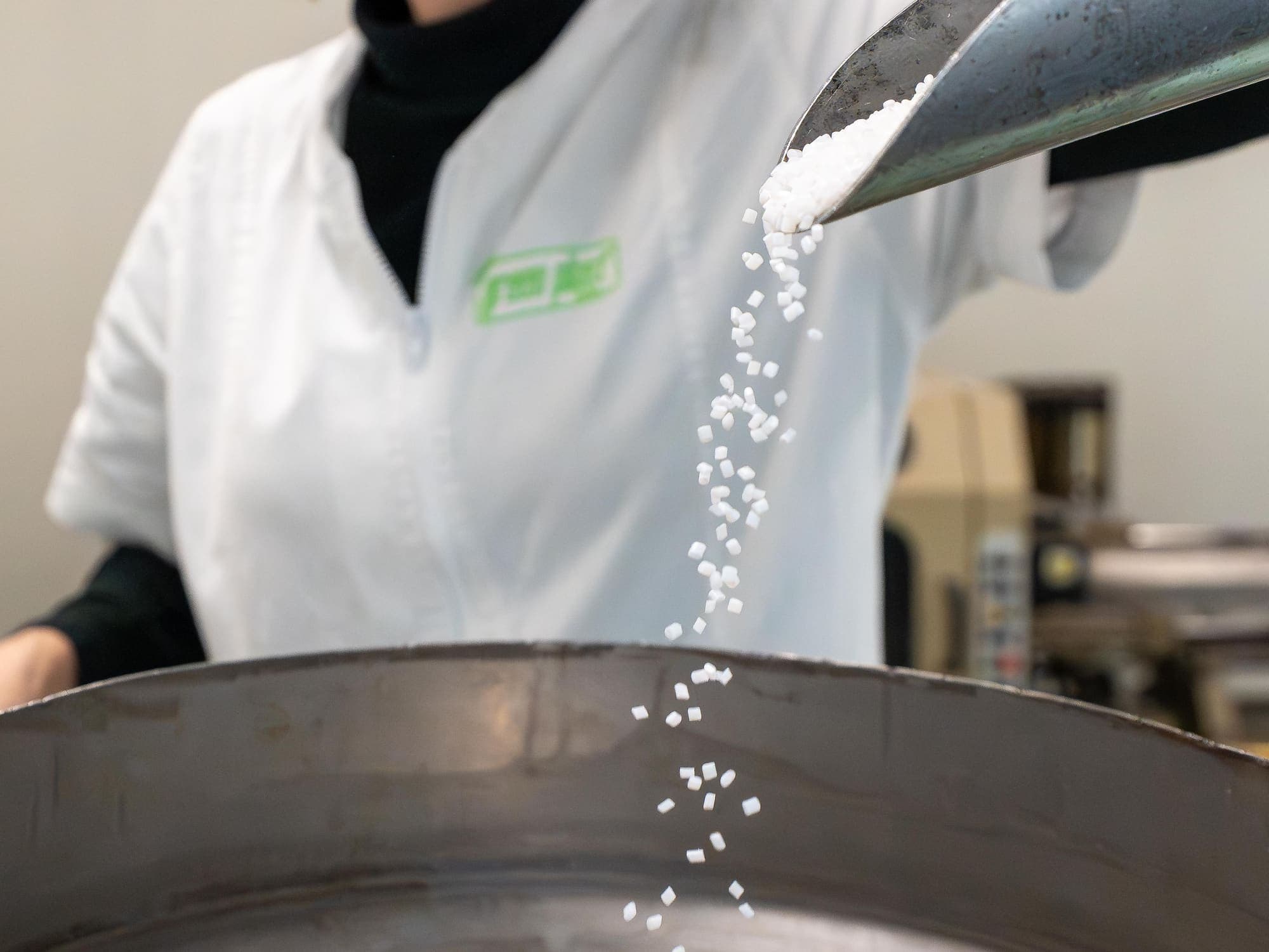 Tecnico in camice Green Plast versa granuli in apparecchiatura di analisi